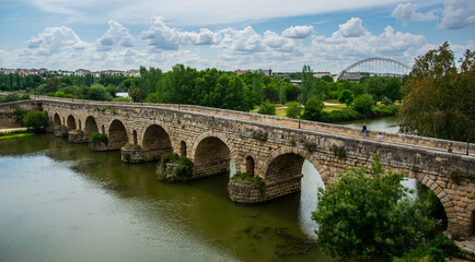 Fototapeta na wymiar En primer término, el Puente Romano, más lejos la vegetación del río Guadiana y al fondo el Puente Lusitania de la ciudad de Mérida, España