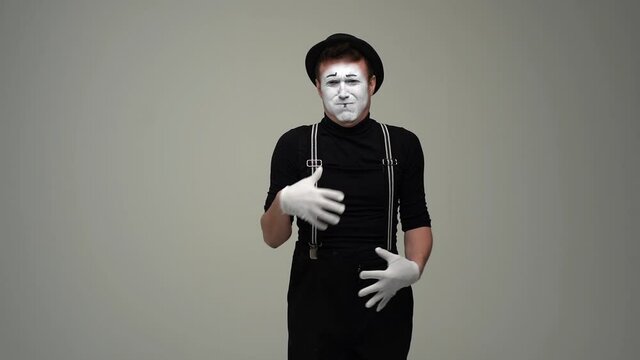 Portrait of sick male mime feeling bad, starts to throw up and leaves the frame. Talented actor wearing hat and gloves showing pantomime on white isolated background. Shooting in slow motion.