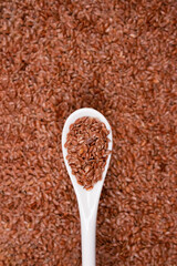 Top view on spoon with flax seeds against linseed background with copy space - healthy eating or skin care concept. Top benefits of linseed in medicine and cosmetology. Selective focus, vertical image