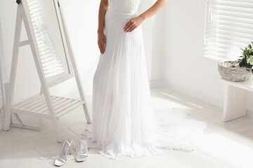 Fototapeta na wymiar Young bride in beautiful wedding dress near mirror indoors, closeup