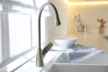 Water drops falling down from tap in kitchen