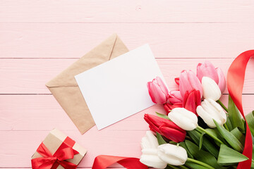 Greeting card and envelope with colorful spring tulips top view over pink wooden background