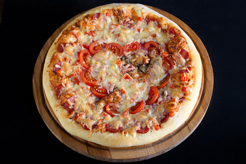 Pizza with pepperoni, tomatoes, mozzarella, on wooden board on black background. Valentines Day concept, soft focus