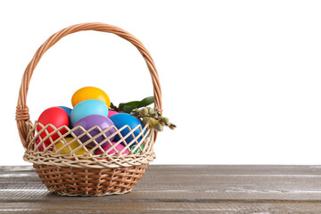 Colorful Easter eggs in wicker basket on wooden table against white background