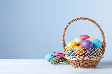 Colorful Easter eggs in wicker basket and willow branches on white wooden table. Space for text