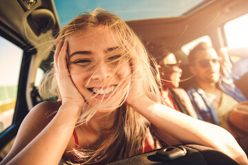 Portrait of young woman travel with her friends, sitting in rear seat and having lots of fun on a road trip.