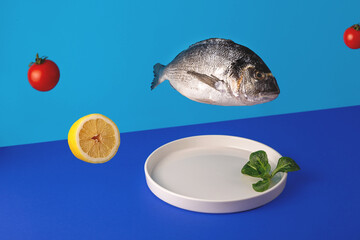 Antigravity dorado fish, green leaves and cherry tomatoes fly over a plate on a bright blue background. Modern trending food photography