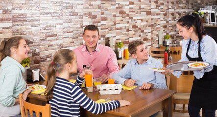 happy brunette waitress serving cheerful family in comfy family cafe