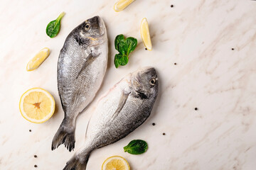 Dorado fish, lemon and green leaves on marble table with water drops and black pepper