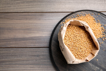 Mustard seeds in paper bag on wooden table, flat lay. Space for text