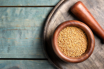 Pestle and mortar with mustard seeds on wooden table, flat lay. Space for text