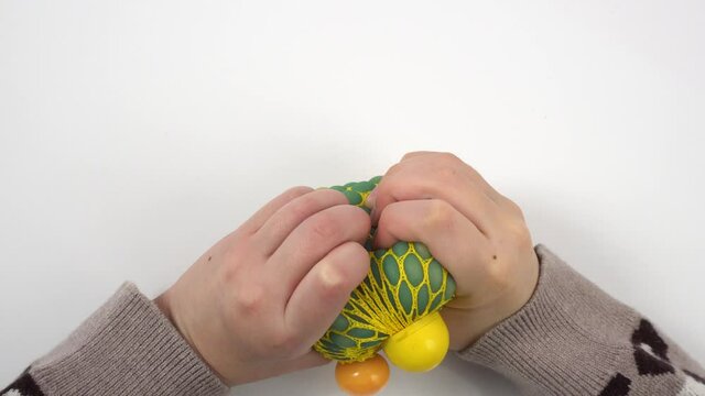 Child's hands squeeze stress ball on white table background. Little girl squeezing green and yellow anti-stress toy.