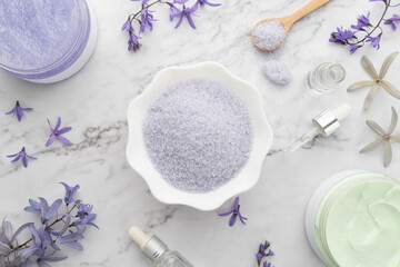 Fototapeta na wymiar Natural spa body scrub products set. Sea salt in bowl with sugar scrub, moisture cream, essential oils and violet flowers on marble table. DIY skin care routines for healthy skin. Flat layout.