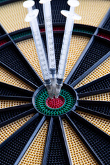 A closeup of dartboard with syringe in the red center, bulls eye. A concept for corona virus pandemic and mass vaccination  in the world. Stop the spread of covid 19