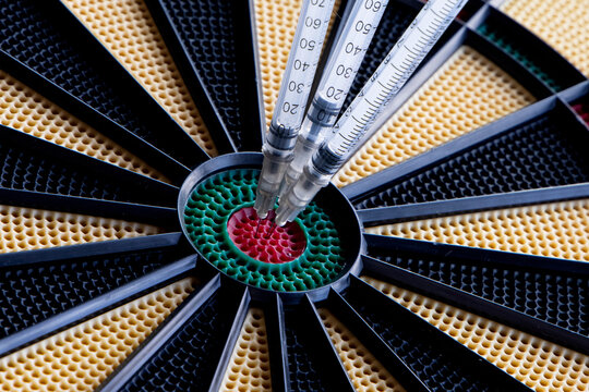 A Closeup Of Dartboard With Syringe In The Red Center, Bulls Eye. A Concept For Corona Virus Pandemic And Mass Vaccination  In The World. Stop The Spread Of Covid 19