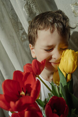 Toddler boy is holding lush bouquet of red and yellow tulips, making faces and smiling funny. vertical, selective focus