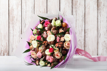 Beautiful bouquet of flowers and chocolate candies on white wooden table