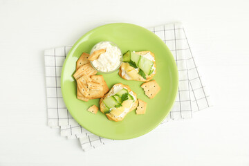 Delicious crackers with cream cheese, cucumber and parsley on white wooden table, top view