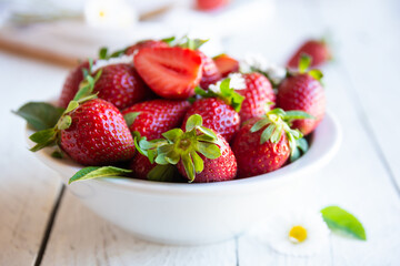 Fresh strawberries in white bowl with leaves and flowers