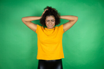 African american woman over green background suffering from headache desperate and stressed because pain and migraine with her hands on head 