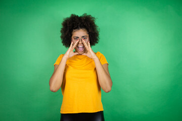 African american woman wearing orange casual shirt over green background shouting and screaming loud to side with hands on mouth