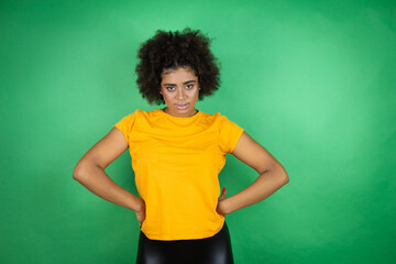 African american woman wearing orange casual shirt over green background skeptic and nervous,...