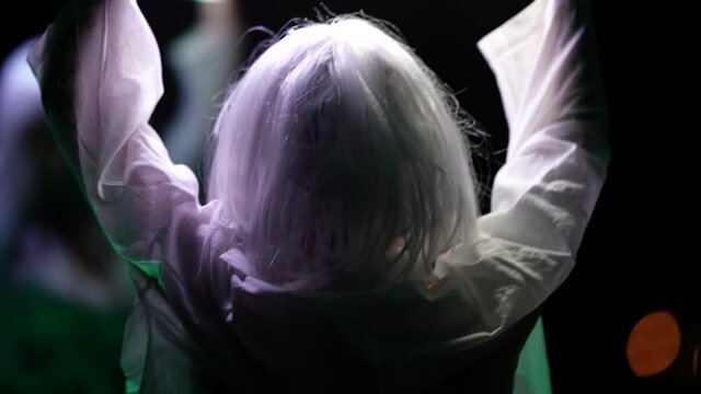 eccentric young lady dressed white clothes and white wig is dancing with laps in darkness, go-go dance show