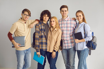 Portrait of a group of young smart girls and boys students in jeans and shirts with backpacks on their shoulders and textbooks in their hands on a gray wall background. Concept of education.