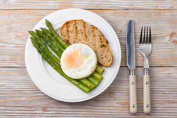 Asparagus with scrambled eggs and buckwheat bread on a plate, top view