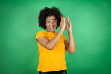 African american woman wearing orange casual shirt over green background clapping and applauding...