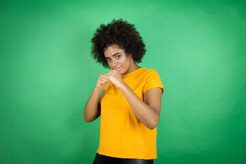 African american woman wearing orange casual shirt over green background Punching fist to fight, aggressive and angry attack, threat and violence