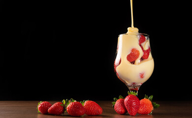Strawberries, crystal bowl with strawberries and condensed milk on a table, black background,...