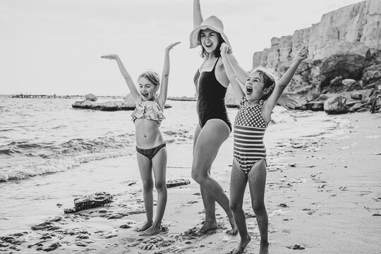 Happy young mother and her little daughters on the seashore in bathing suits.