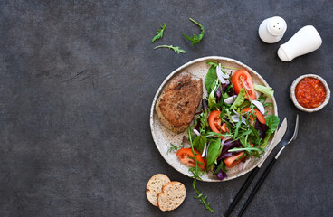 Grilled beef steak medium with mix salad and tomatoes on a black concrete background.