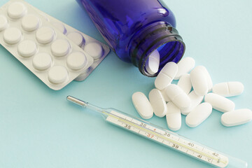 thermometer and medicine pills on blue background, health care concept