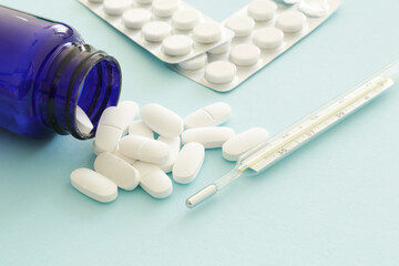 thermometer and medicine pills on blue background, health care concept