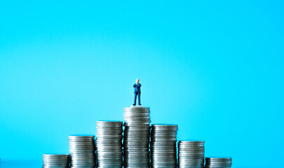 Miniature people businessman on top of stacks coins in money communication on blue background