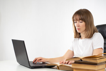 Woman is engaged in training on her own. She uses a laptop and books for self study. Student is engaged in self study. Portrait of a female student next to a computer. Books and laptop in self study