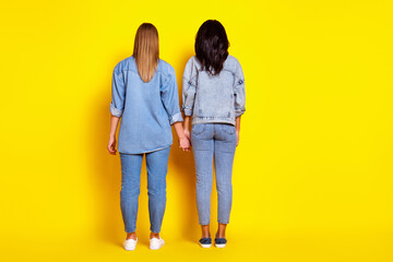 Full length rear photo of two ladies standing hold each other arms isolated on yellow color background