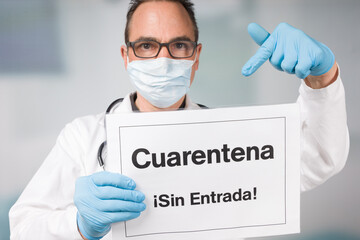 Doctor with medical face mask and medical gloves pointing to a spanish quarantine sign in front of...