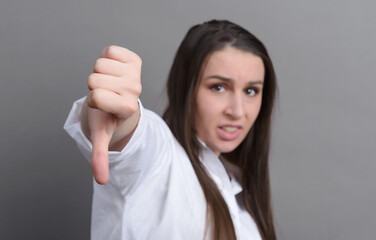 young woman in a white shirt shows a sign with her finger down, bad on a gray background