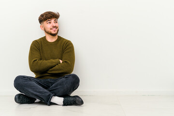 Young Moroccan man sitting on the floor isolated on white background smiling confident with crossed arms.