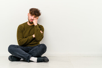 Young Moroccan man sitting on the floor isolated on white background who feels sad and pensive, looking at copy space.