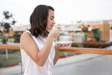 A young woman holds a saucer in her hand and enjoys a cup of morning coffee.