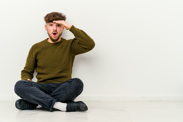 Obraz premium Young Moroccan man sitting on the floor isolated on white background shouts loud, keeps eyes opened and hands tense.