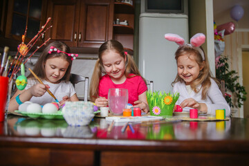 Three girls coloring Easter eggs at home at the kitchen table