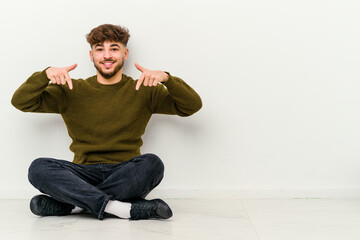 Young Moroccan man sitting on the floor isolated on white background points down with fingers, positive feeling.