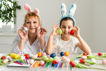 Easter concept. Grandmother with granddaughter are holding Easter eggs at home