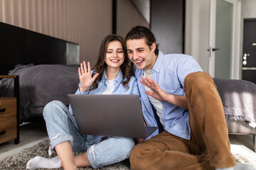 Young couple video chatting sitting on floor at home in bedroom