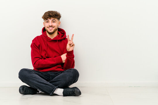 Young Moroccan man sitting on the floor isolated on white background showing number two with fingers.